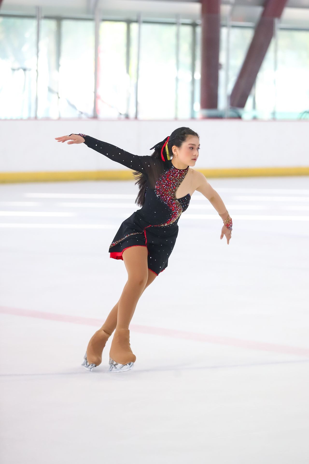 Figure skater performing on an ice rink in a black and red outfit with one arm extended.